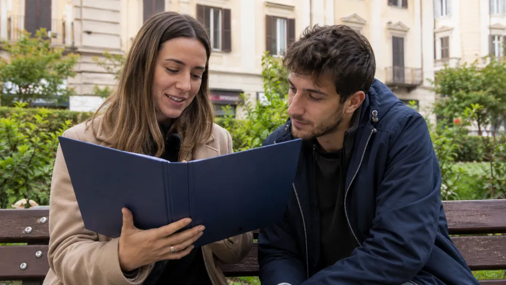 Due persone consultano una guida BauDar cartacea sedute su una panchina